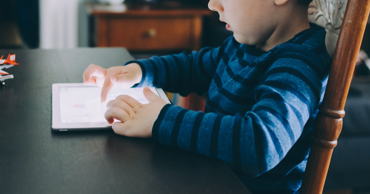 A young boy sitting at a table focused on a tablet computer, representing guided AI tool use for children ages 4-8 in Shanghai